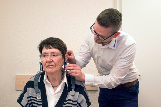 Ein Hörakustiker passt einer Seniorin ein Hörgerät im Hörtestraum an.