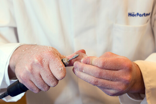 Ein Hörakustiker bearbeitet ein Hörgerät handwerklich mit speziellem Werkzeug.